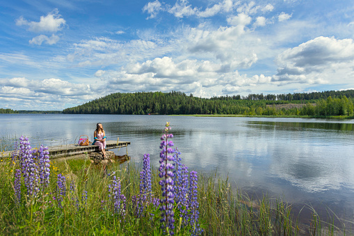 A woman sitting on a jetty and enjoying the summer sunlight. Lake Saxen in Dalarna, Sweden.