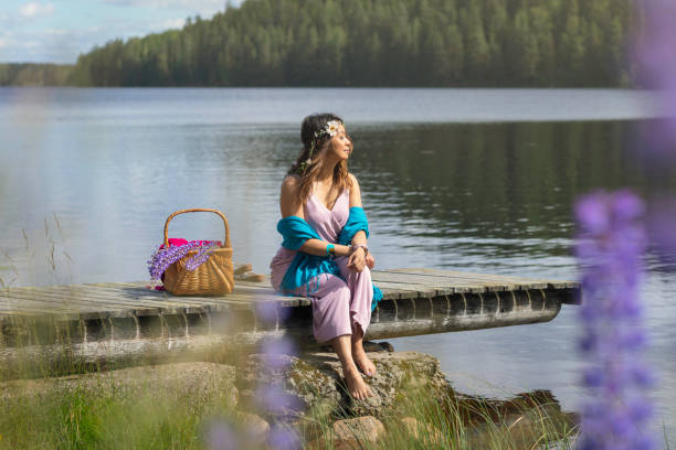 A woman relaxing on a jetty at the edge of a lake with eyes closed in the sunlight.