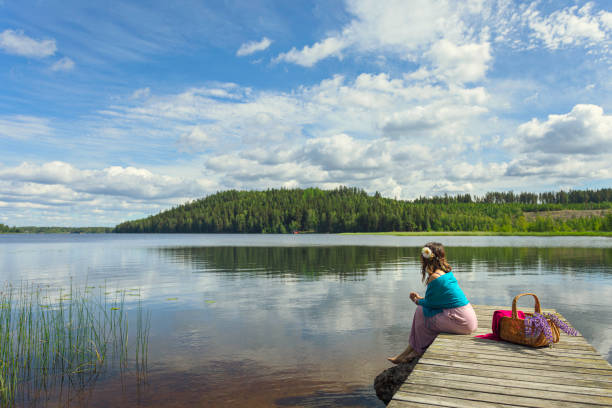 Woman sitting on a jetty by a lake in summer and relaxing. Lake Saxen in Dalarna, Sweden.