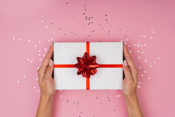 istock Women hands holding a gift or gift box decorated with confetti on a pink pastel table top view. Flat composition for birthday or wedding. 1248992189