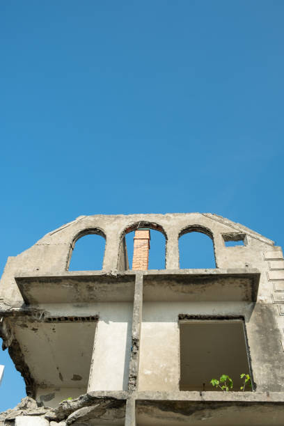 Dilapidated residential building, against the blue sky. Plastered walls, building frame. Red brick chimney. Empty window openings. Destroyed floors.
