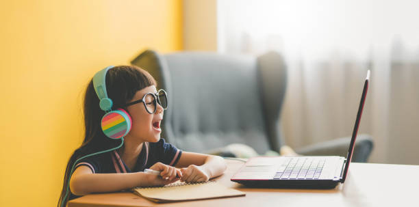 Young Asian Cute girl studying with laptop at home during pandemic Image of Young Asian cute girl at home sitting on the table, using laptop, studying. Study at home during pandemic concept. E learning. home schooling homework computer learning stock pictures, royalty-free photos & images