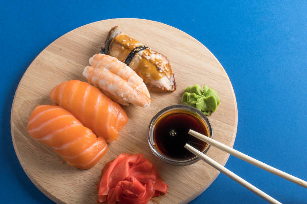 köstliches appetitliches nigiri-sushi-set auf holztellern mit sojasauce und essstäbchen serviert. wohnung lag auf blauem hintergrund - chopsticks soybean japanese cuisine blue stock-fotos und bilder