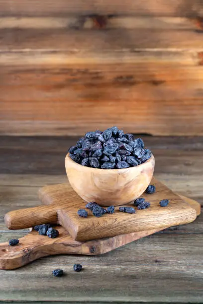 Black Raisins in the bowl on wooden rustic background