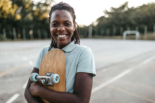Smiling African woman with skateboard on playground