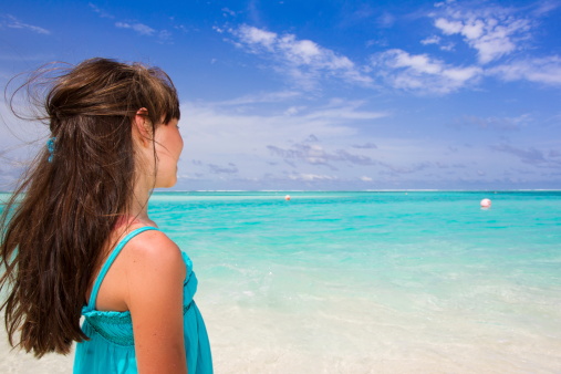 Outdoor portrait of a little Caucasian young girl with brunette long hair watching the ocean in front of blue sky background.