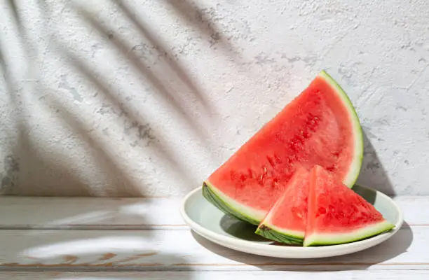 Photo of Fresh watermelon at the sun with tropical leaves shadows