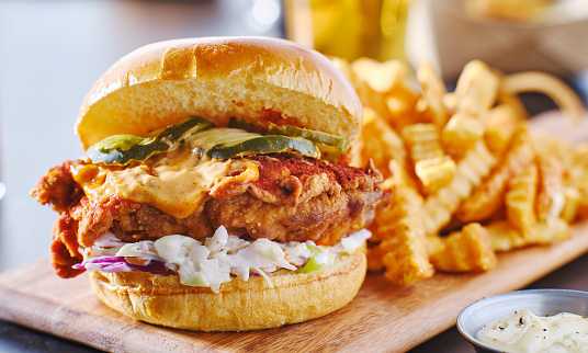 spicy nashville hot chicken sandwich with coleslaw and pickles on wooden cutting board