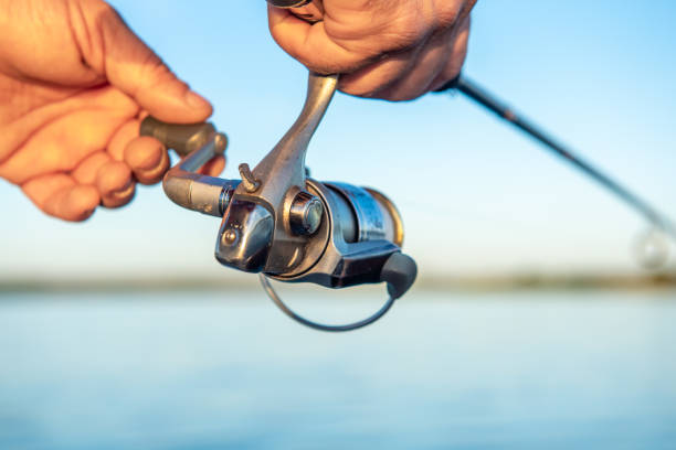 mãos de homens segurando uma vara de pesca e torcer a alça do carretel de pesca. profundidade de campo rasa, foco suave - fishing rod fishing fishing reel casting - fotografias e filmes do acervo