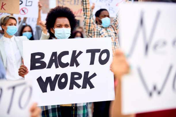 istock Black woman wearing protective face mask while holding 'back to work' sign during anti-lockdown protest. 1249018234