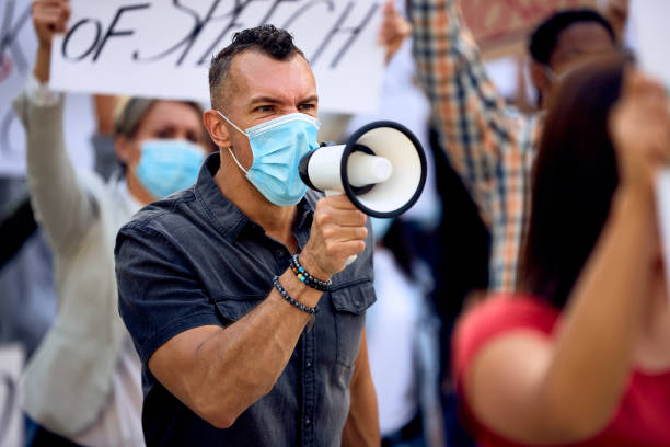 istock Caucasian man wearing protective face mask while shouting through megaphone on anti-lockdown protest. 1249018398