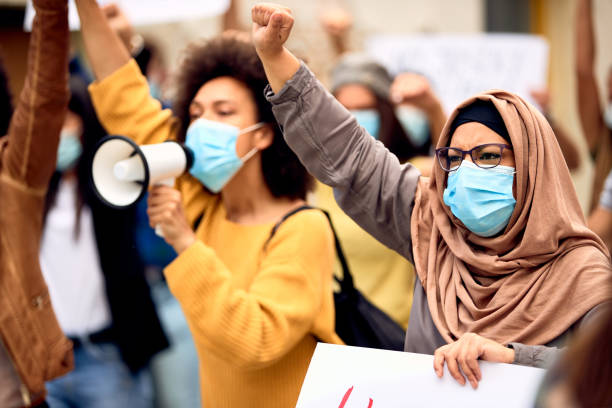 Muslim woman wearing protective face mask while being on a protest against racial discrimination. Muslim woman wearing protective face mask and supporting anti-racism movement with group of people on city streets. social justice concept photos stock pictures, royalty-free photos & images