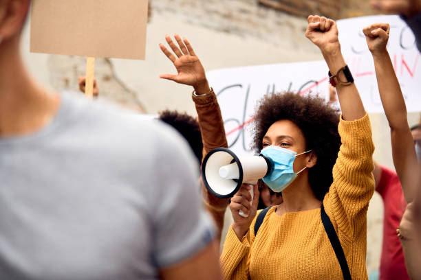 istock Young black woman wearing protective face mask while shouting through megaphone on anti-racism solidarity protest. 1249019325