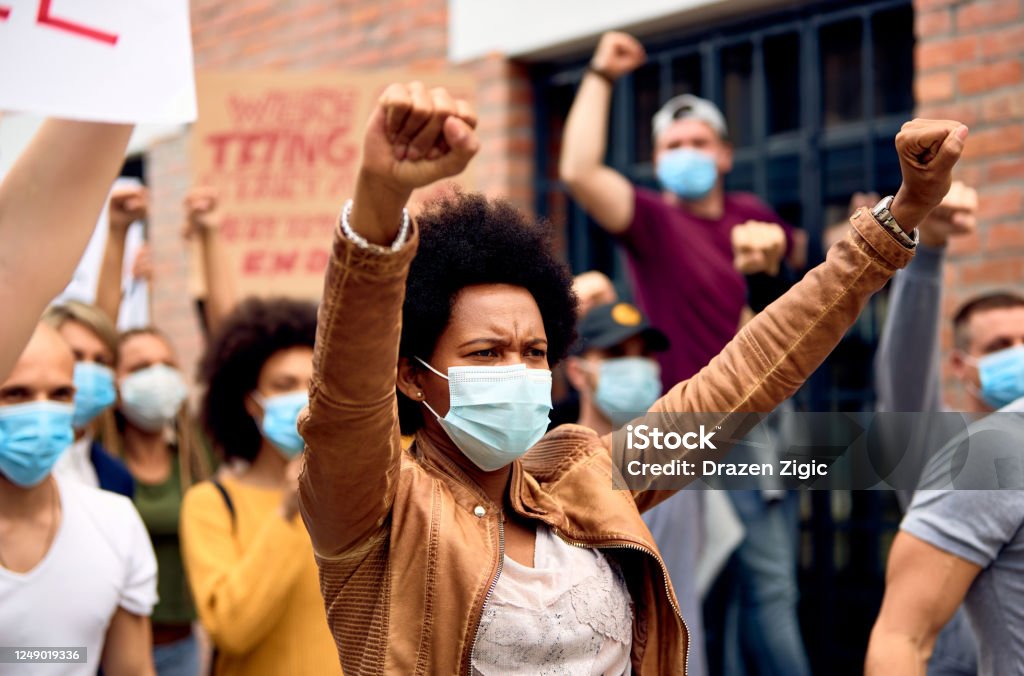 African American woman wearing protective face mask while protesting with arms raised on city streets. Black woman with raised fists wearing protective face mask while supporting anti-racism demonstrations. Anti-racism Stock Photo