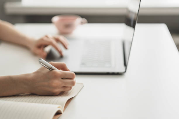 istock A young woman works on a laptop and takes notes in a notebook. 1249019649
