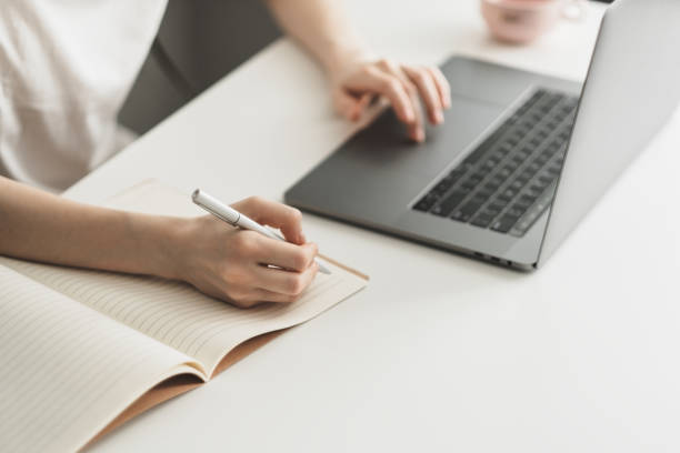 istock A young woman works on a laptop and takes notes in a notebook. 1249019771