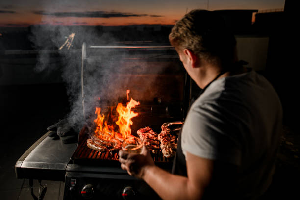 chef maschio che usa pinngs capovolge delicatamente pezzi di carne sul barbecue in fiamme - spit roasted barbecue grill barbecue pork foto e immagini stock