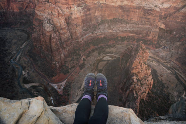 Angel's Landing trail, Zion National Park, Utah, USA. Woman tourist sitting on the cliff edge with dangling legs.