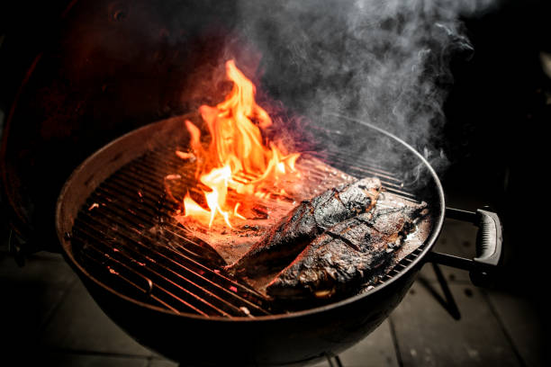 Two fish prepare on grill of round barbecue.