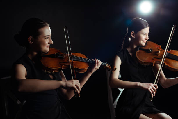 istock happy attractive musicians playing on violins on dark stage with back light 1249020940