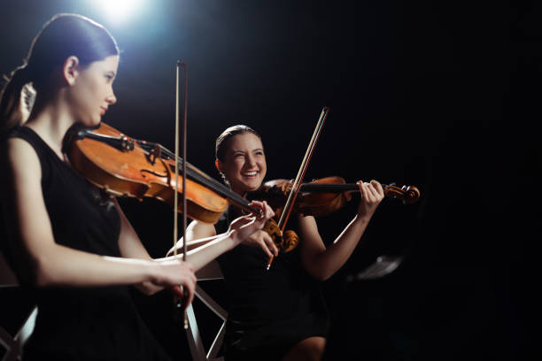 istock laughing female musicians playing on violins on dark stage with back light 1249020947