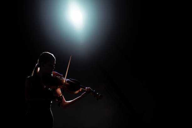 silueta de la músico femenina tocando en el violín en el escenario oscuro con la luz de la espalda - violin women violinist music fotografías e imágenes de stock