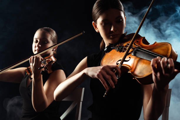istock beautiful musicians playing on violins on dark stage with smoke 1249020981