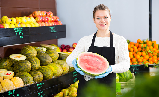 Young woman offering watermelon and other fresh fruits on the market