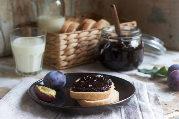 Bread toast with plum jam, served with milk and plums on a wooden background. Rustic style.