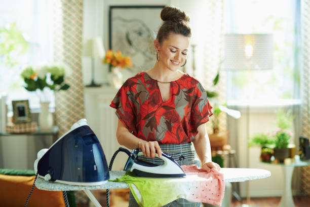 smiling housewife ironing in modern house in sunny day - estereótipo de dona de casa imagens e fotografias de stock