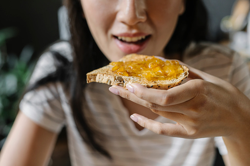 Smiling young Asian woman eating bread, jam and butter for breakfast, a close up.