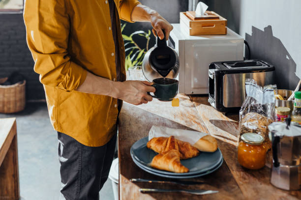 Happy Asian Man Making Tea in the Kitchen in the Morning Smiling man enjoying a cup of tea in the morning. toaster stock pictures, royalty-free photos & images