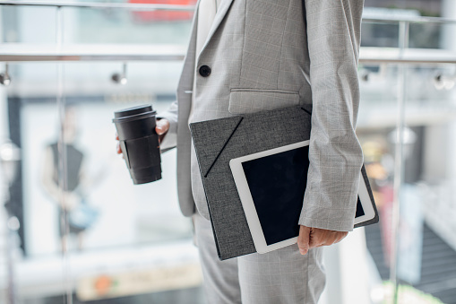 Unrecognisable elegant businesswoman standing outdoors and holding a coffee and digital tablet and folder.