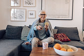 Senior woman watching TV and snacking an apple at home