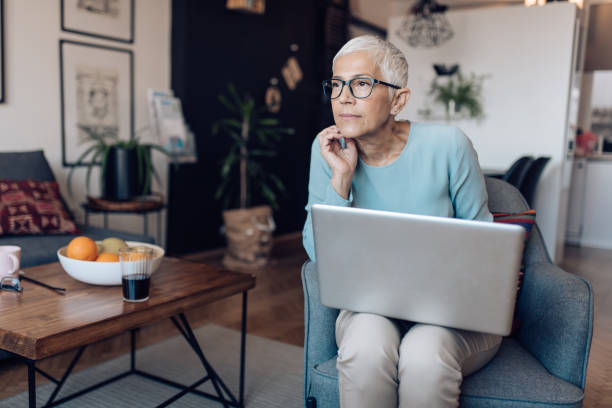 mujer mayor cuidadosamente sentada mientras busca un trabajo en línea - thinking professional occupation unemployment job search fotografías e imágenes de stock