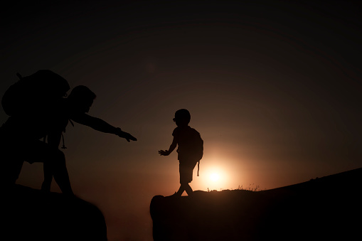 silhouette of man and boy on the edge of the cliff at sunset