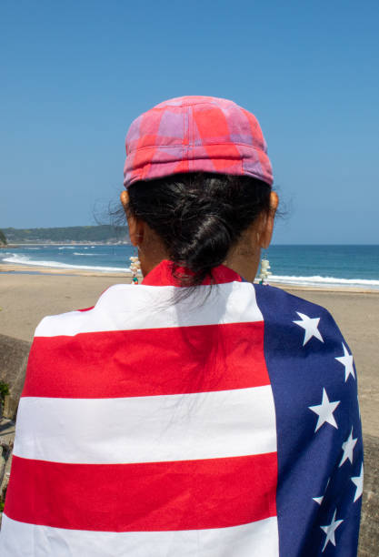 Asian lady wearing various county flags on her back while looking out to the ocean in Japan.