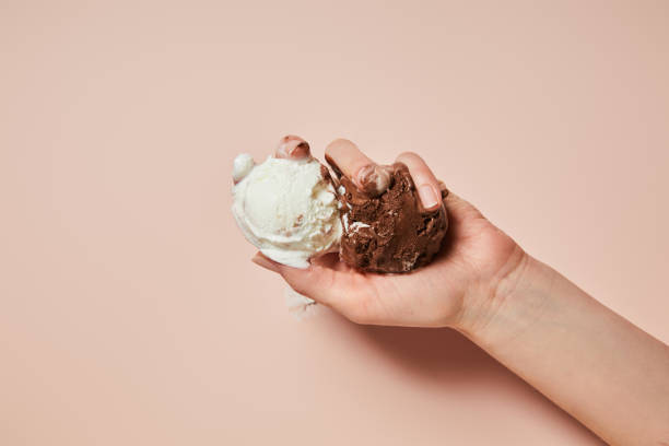 cropped view of woman holding melted brown and white ice cream on pink background