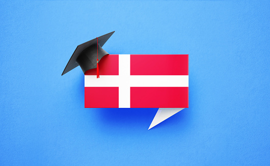 Graduation cap sitting over a speech bubble textured with Danish flag on blue background. Horizontal composition with copy space. Front view. Study in Denmark concept.