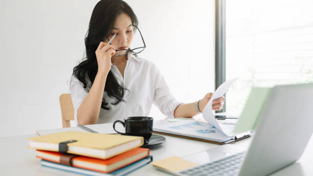 istock Young asian entrepreneur cogitating thinking making important decision at workplace. Concentrated serious office worker millennial woman analysing results 1249099485