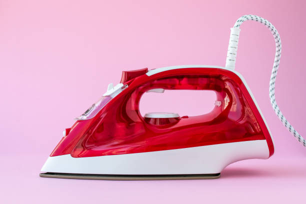 istock Red plastic iron on pink background. Appliance for ironing clothes, housework concept. 1249101745