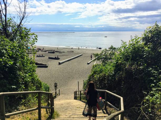 A Young Woman Walking Down The Stairs Facing Outwards Towards Wreck Beach  In Vancouver Bc It Is A Beautiful Summer Day With The Ocean And People In  The Distance Stock Photo -