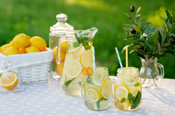 istock Lemonade refreshing drink in a jug and jars with lemons, fresh mint and ice with a basket with lemons and kumquat on a garden table. Summer outdoor picnic. Soft selective focus. 1249102811