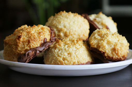 Stock photo of freshly baked coconut macaroons cakes dipped in milk chocolate stack up on white plate, made with desiccated coconut mixed with egg whites, sugar, butter and vanilla flavour, cookie / biscuits dipped in melted chocolate.