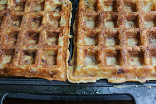 Stock photo of savoury potato waffles cooking in waffle iron / waffle maker, healthy breakfast snack made of grated potato mixed with egg and whole wheat flour. crispy omelet / omelette waffle ready to eat. imagen de gofres de patata salada cocinando en waffle plancha / waffle maker, aperitivo de desayuno saludable hecho de patata rallada mezclada con huevo y harina de trigo integral. tortilla crujiente / gofre de tortilla listo para comer.