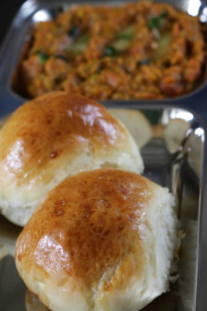 Stock photo of traditional Indian / Mumbai street food Pav bhaji dish served in a stainless steel compartment plate with freshly baked pav / bread rolls. Bhaji / gravy is made from mixture of pepper, tomato, green peas, potato, onion and flavoured with different spices. This dish is served with chopped raw onion, slice of lemon and butter on the side. elevated view imagen de la comida tradicional india / mumbai pav bhaji plato servido en placa compartimiento de acero inoxidable con pavimento recién horneado / panecillos. bhaji / salsa se sirve con cebolla cruda picada, rodaja de limón y mantequilla en el lado, vist