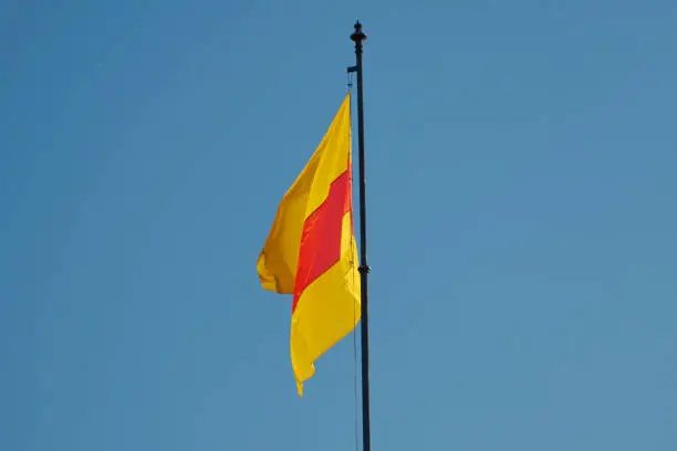 Close-up of yellow and red flag of Baden fluttering in the wind against blue sky on a sunny day. Heraldic colours of the former German state of Baden, located on top of the baroque castle in Rastatt