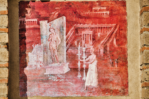Looking at ancient wall painting at the Tempel of Isis in the city of Pompeii. When the Temple of Isis was discovered by excavators its decoration and furnishings were almost intact, thereby contributing decisively to introduce Pompeii to the world. Pompeii is an ancient Roman city that was buried under 4 to 6 m (13 to 20 ft) of volcanic ash and pumice in the eruption of Mount Vesuvius in AD 79. Today Pompeii is a UNESCO World Heritage Site and is one of the most popular tourist attractions in Italy.
