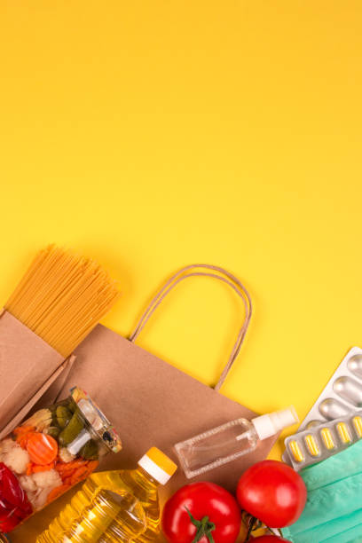 istock Vertical composition with food and medicaments donations on yellow background with copyspace. Pasta, fresh vegatables, canned food, baguette, disinfecting spray and masks. Donation food concept 1249115734