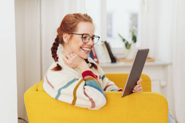 Smiling happy young woman reading on a tablet stock photo